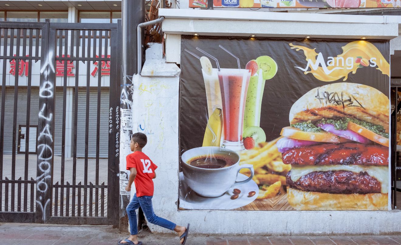 Un niño corre delante de un cartel de comida rápida hacia una tienda de caramelos en el centro de Santiago, Chile (UNICEF/UN0805425/Goupil)